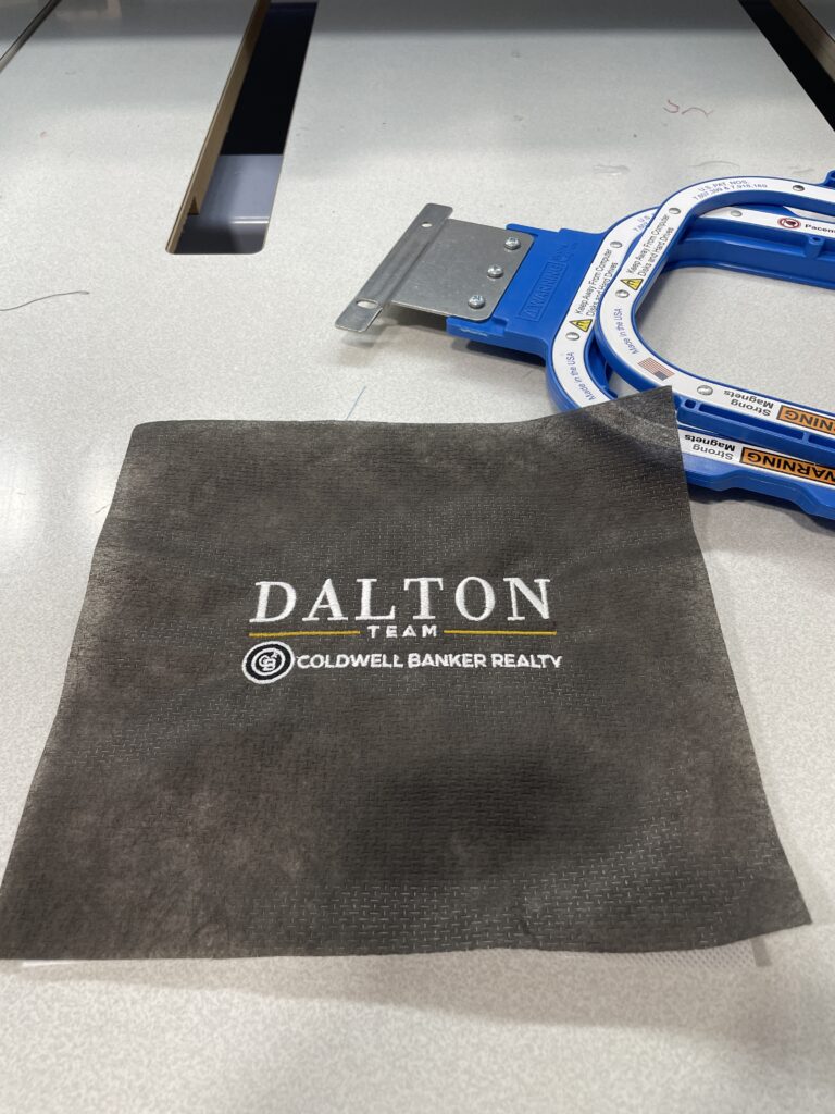 Close-up of an embroidered company logo stitched on a grey garment